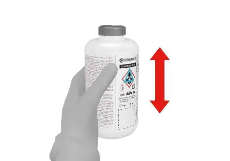 Shaking the sealant bottle before installation in the Kia EV2 emergency kit compressor